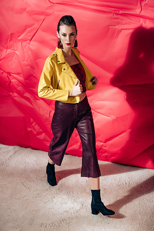 stylish model posing in yellow leather jacket on red background for fashion shoot