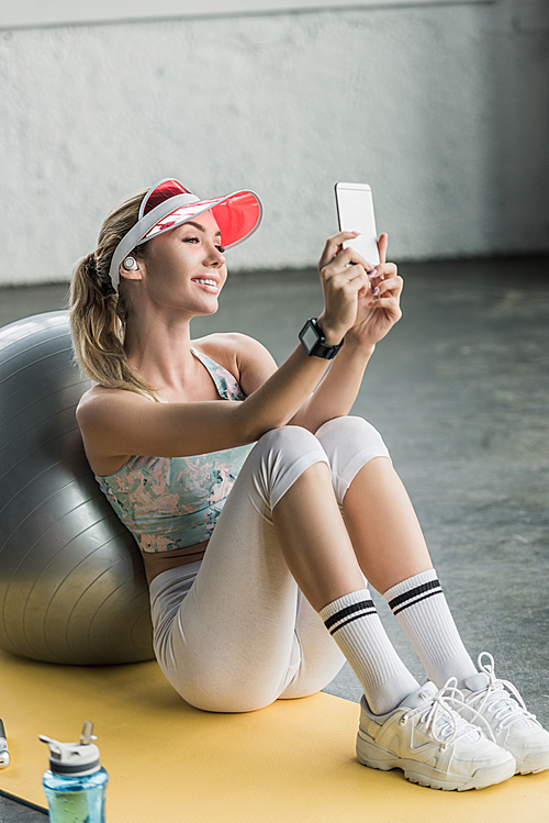 happy female athlete with smartwatch taking selfie on smartphone near fitness ball at gym