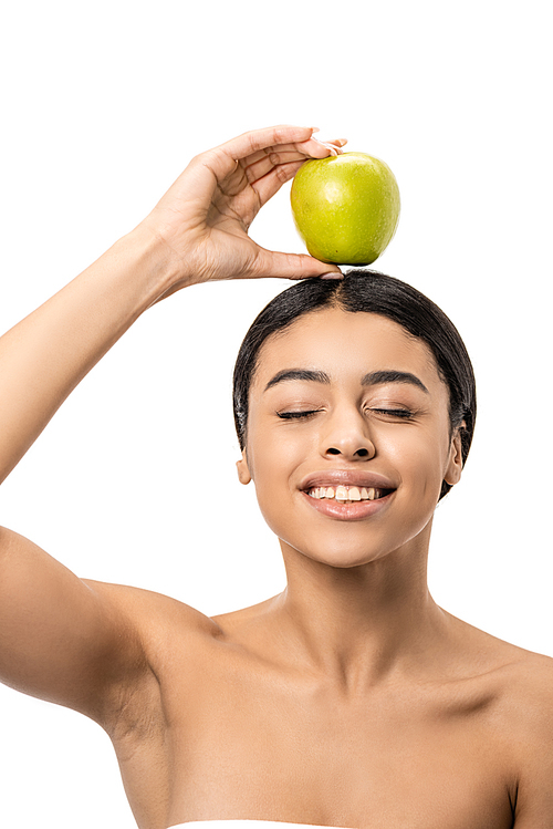 happy naked african american girl with closed eyes holding green apple on head isolated on white