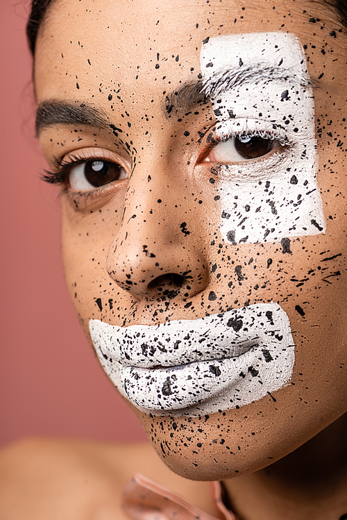 beautiful african american woman with white paint and brown splashes on face  isolated on pink