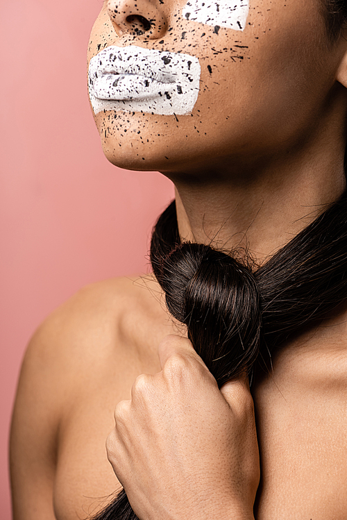 cropped shot of young african american woman with paint on face and brunette hair around neck isolated on pink