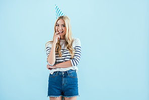 Girl in party hat biting finger isolated on blue
