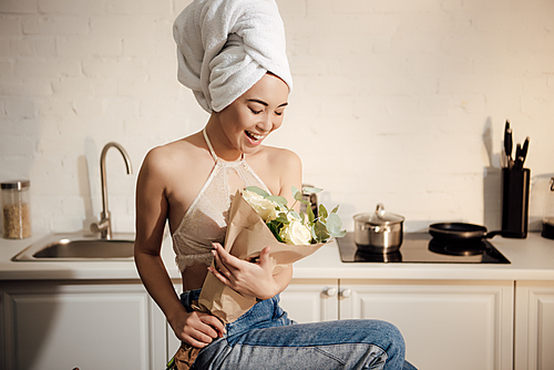 surprised happy asian girl with towel on head holding bouquet of white rose flowers at home