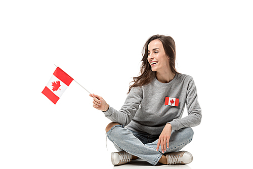 smiling woman with maple leaf badge sitting and holding canadian flag isolated on white