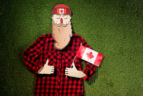 cardboard man in plaid shirt holding canadian flag and showing thumbs up signs on green grass background
