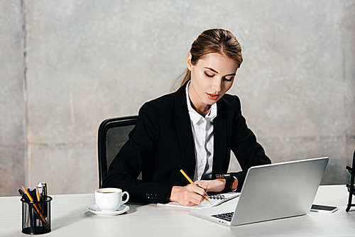 young concentrated businesswoman sitting at workplace and making notes