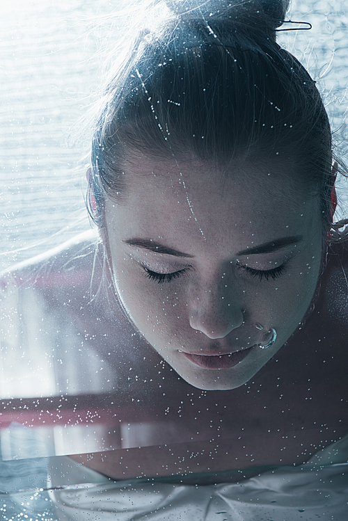 close up of young woman diving underwater with closed eyes