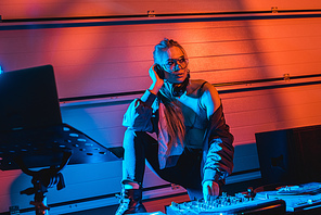 thoughtful dj woman in glasses touching dj mixer while listening music in headphones