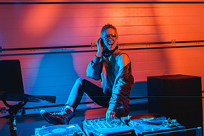 cheerful dj girl in glasses touching dj mixer in nightclub