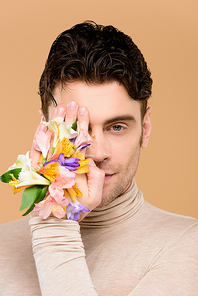 man with alstroemeria flowers on hand covering one eye isolated on beige