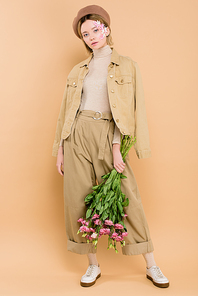 stylish girl in beret holding bouquet with eustoma flowers isolated on beige