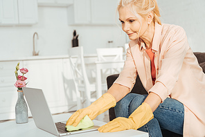 Senior woman in rubber gloves cleaning laptop keyboard