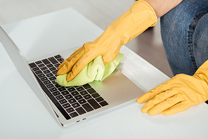 Partial view of woman in yellow rubber gloves cleaning laptop keyboard with rag