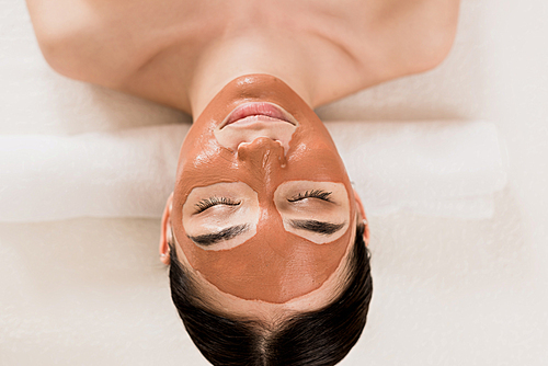 beautiful woman lying with clay mask on face at spa
