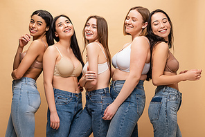 five cheerful multicultural women smiling and posing at camera isolated on beige, body positivity concept