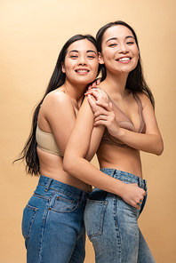 two cheerful multicultural girls hugging and  isolated on beige, body positivity concept