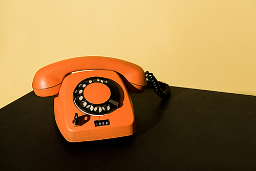 Old orange telephone standing on black surface on yellow background