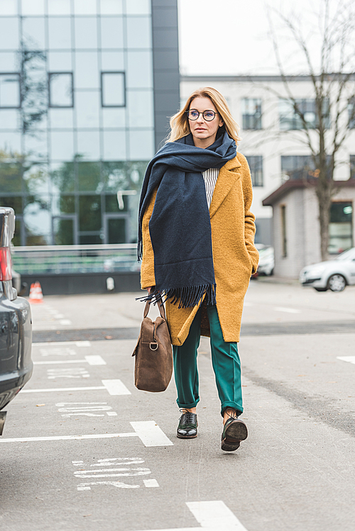 elegant woman in autumn outfit with leather bag walking on parking