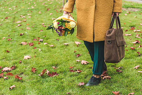 cropped view of stylish woman in yellow coat holding bouquet and leather bag