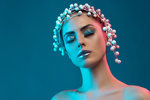 portrait of beautiful woman with hair accessory, winter makeup and glitter posing for fashion shoot, isolated on blue