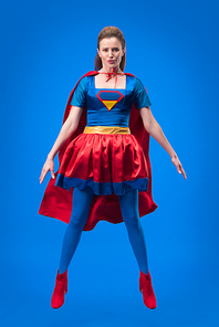 beautiful superwoman in costume jumping isolated on blue