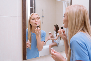 attractive girl applying lips gloss in bathroom