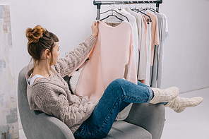 side view of girl sitting on armchair and looking at shirt in hand