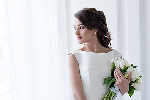 beautiful bride holding wedding bouquet and looking at window