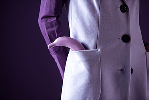 Cropped view of stylish elegant girl posing in purple clothes with banana in pocket, isolated on purple