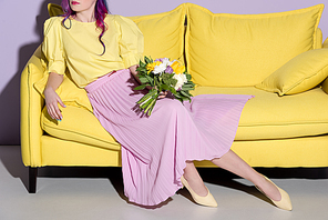 cropped shot of woman sitting on yellow couch with floral bouquet
