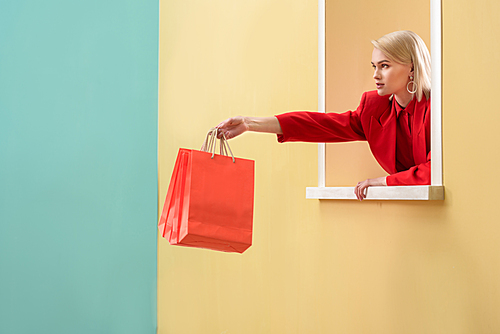 young fashionable woman in red clothing with red shopping bags looking out decorative window