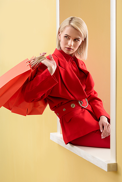 young fashionable woman in red clothing with red shopping bags sitting on decorative window