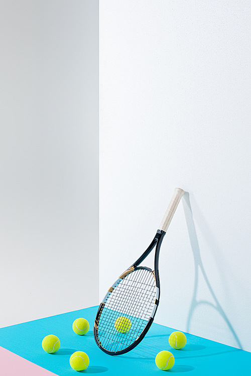 circle of tennis balls on blue around tennis racket at white wall with copy space