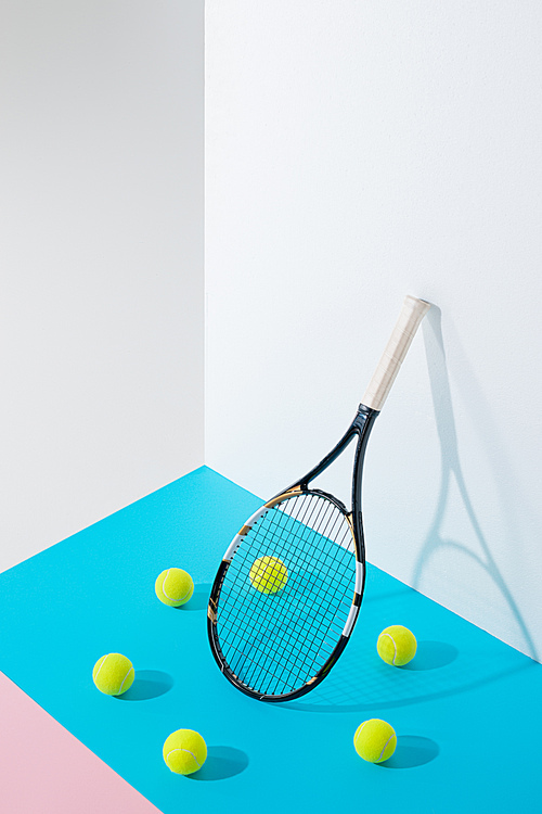 circle of tennis balls on blue around tennis racket at white wall