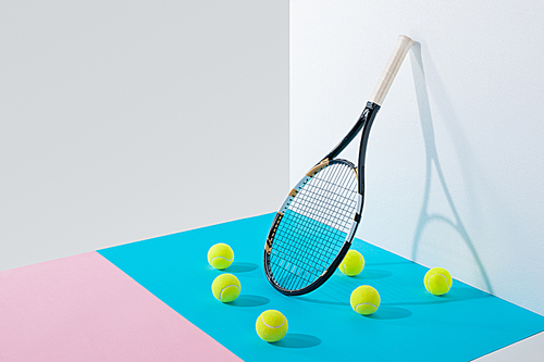yellow tennis balls on blue and pink papers and tennis racket at white wall