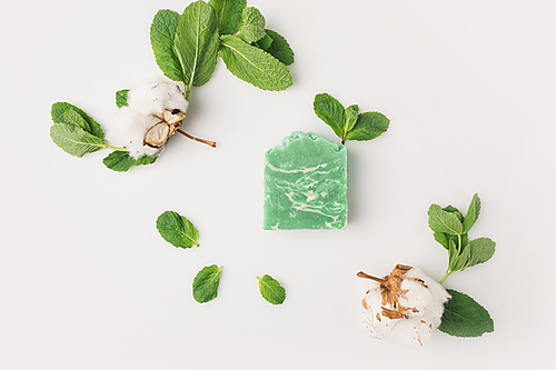 top view of homemade mint soap with leaves and cotton flowers on white surface
