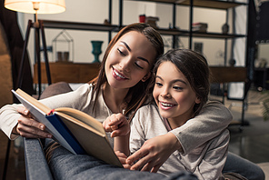 portrait of smiling young mother and daughter reading book together at home
