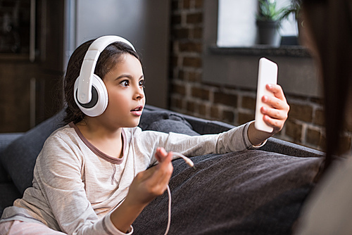 selective focus of shocked child in headphones looking at smartphone in hand at home