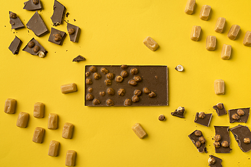 Top view of milk chocolate bar with scattered pieces and iris milk candies isolated on yellow