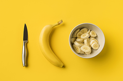 Top view of Plate with cut bananas, ripe banana and knife isolated on yellow