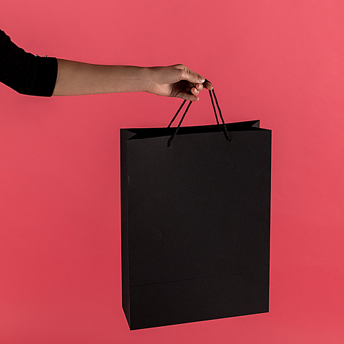 cropped shot of woman holding black shopping bag isolated on red