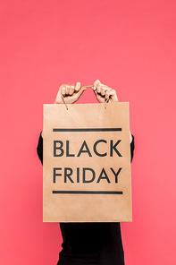 partial view of woman holding shopping bag with black friday lettering in hands isolated on pink