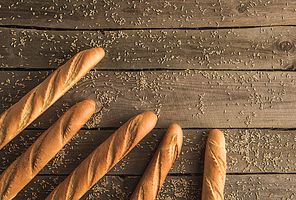 top view of fresh homemade baguettes and wheat grains on wooden table