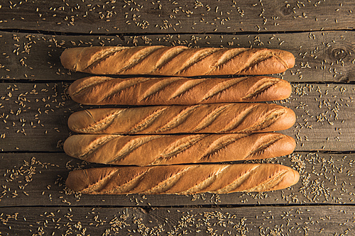 top view of fresh delicious baguettes and wheat grains on rustic wooden table