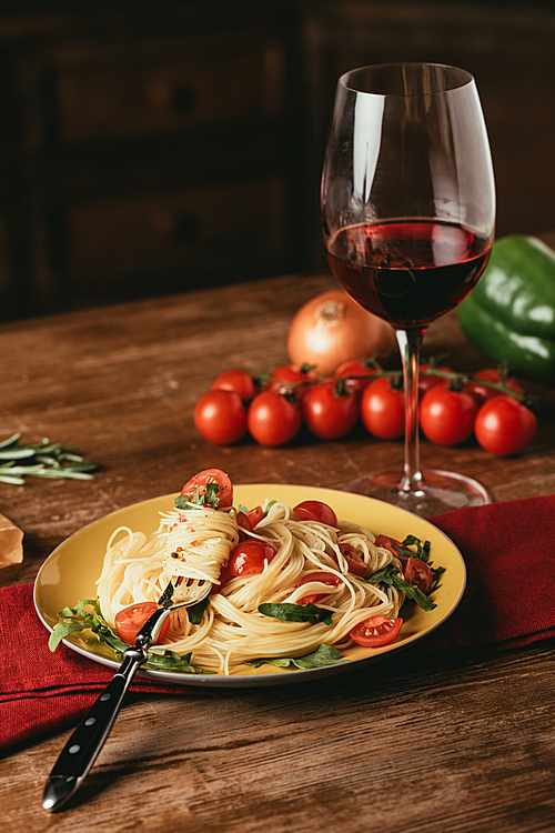 traditional italian pasta with tomatoes and arugula in plate and glass of red wine