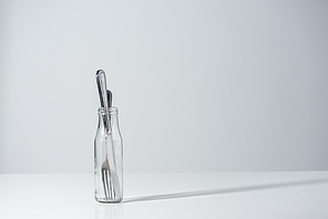 fork and knife in glass bottle with shadow on grey