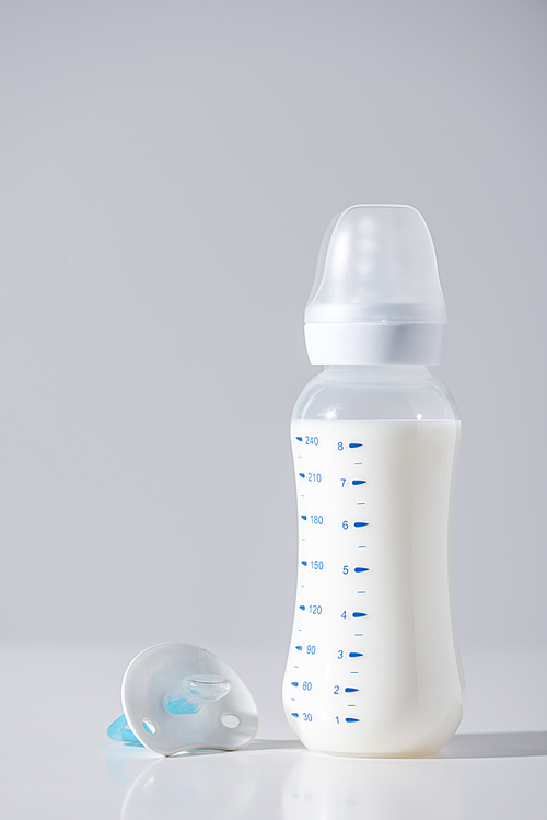 close-up view of plastic bottle with milk and nipple on grey