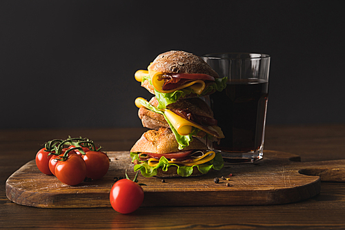 big sandwich with cheese, cherry tomatoes and glass of cola on cutting board