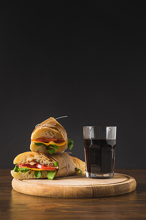 two sandwiches on each other and glass of cola on cutting board
