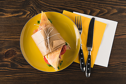 top view of panini on yellow plate with fork and knife on napkins